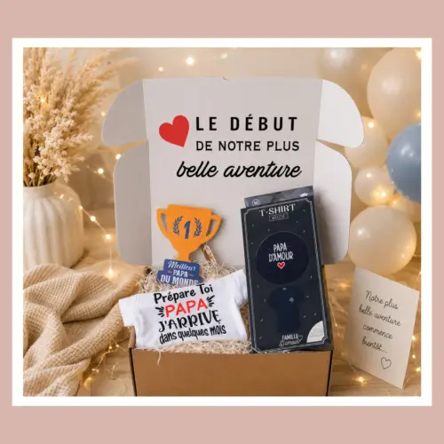 Coffret cadeau d'annonce de grossesse ouvert affichant le message "Le début de notre plus belle aventure" et contenant un body bébé "Prépare-toi papa", un t-shirt brodé "Papa d'amour", un trophée en bois et une carte de vœux